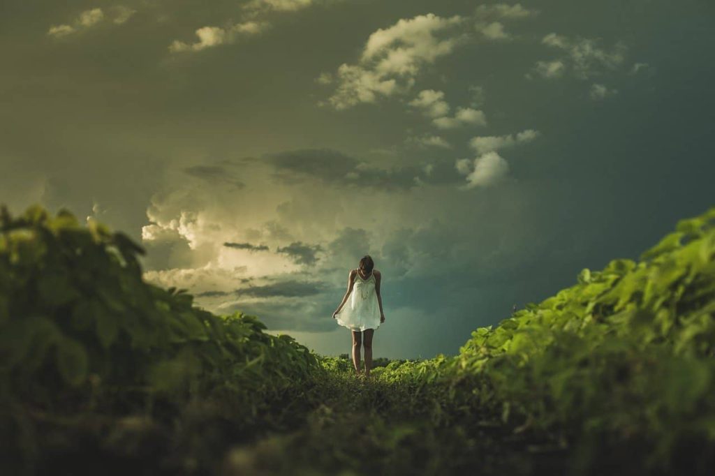 Girl with white dress on grass with clouds behind her