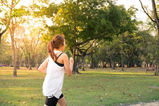 a woman jogging in nature surrounded by green trees