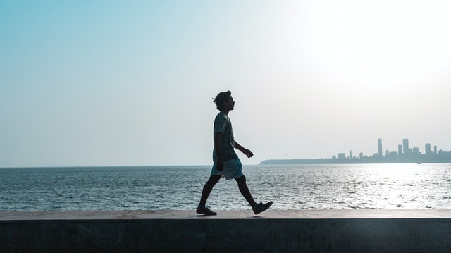 a guy walking mindfully next to the sea with the city view behind the sea