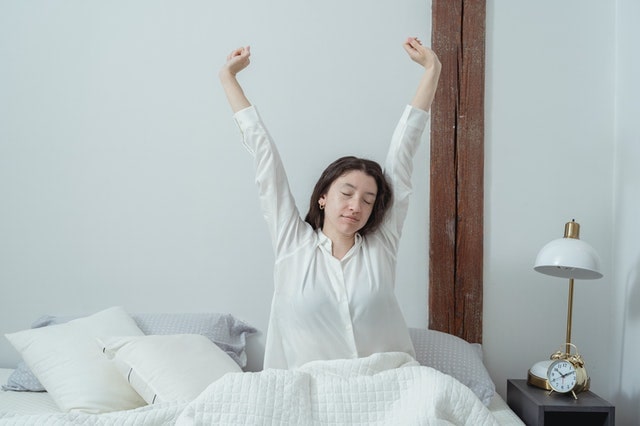 a woman in bed stretching her hands up smiling waking up mindfully