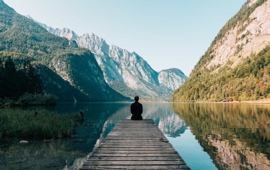 A person sitting down looking at a lake and beautiful mountain view