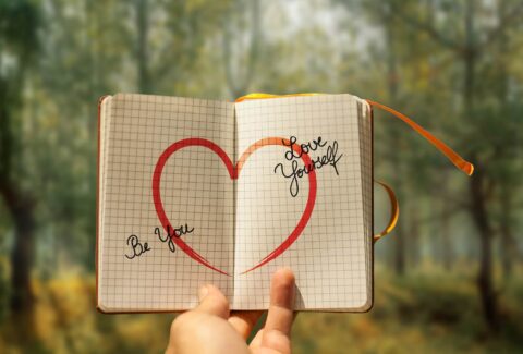 hand holding notebook with heart and self love in forest