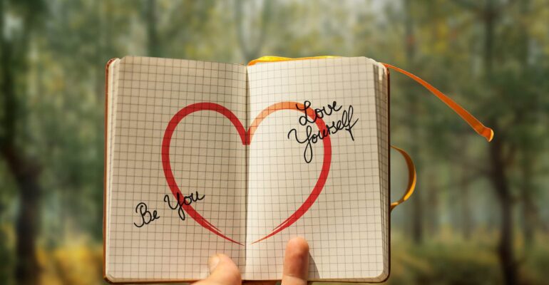 hand holding notebook with heart and self love in forest