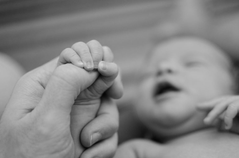 black and white photo of baby holding mum's fingers