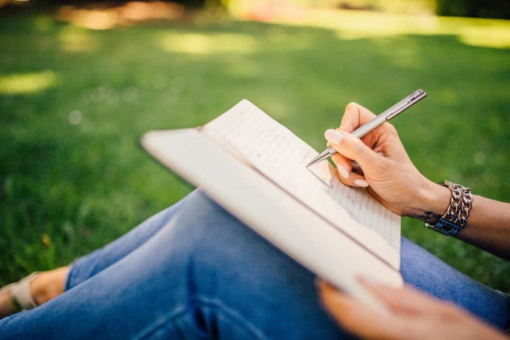 girl sitting down on grass writing on her journal