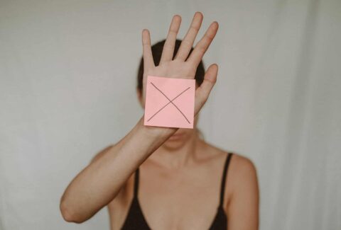 woman holding hand up with a note X covering her face