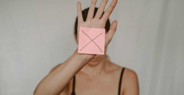 woman holding hand up with a note X covering her face