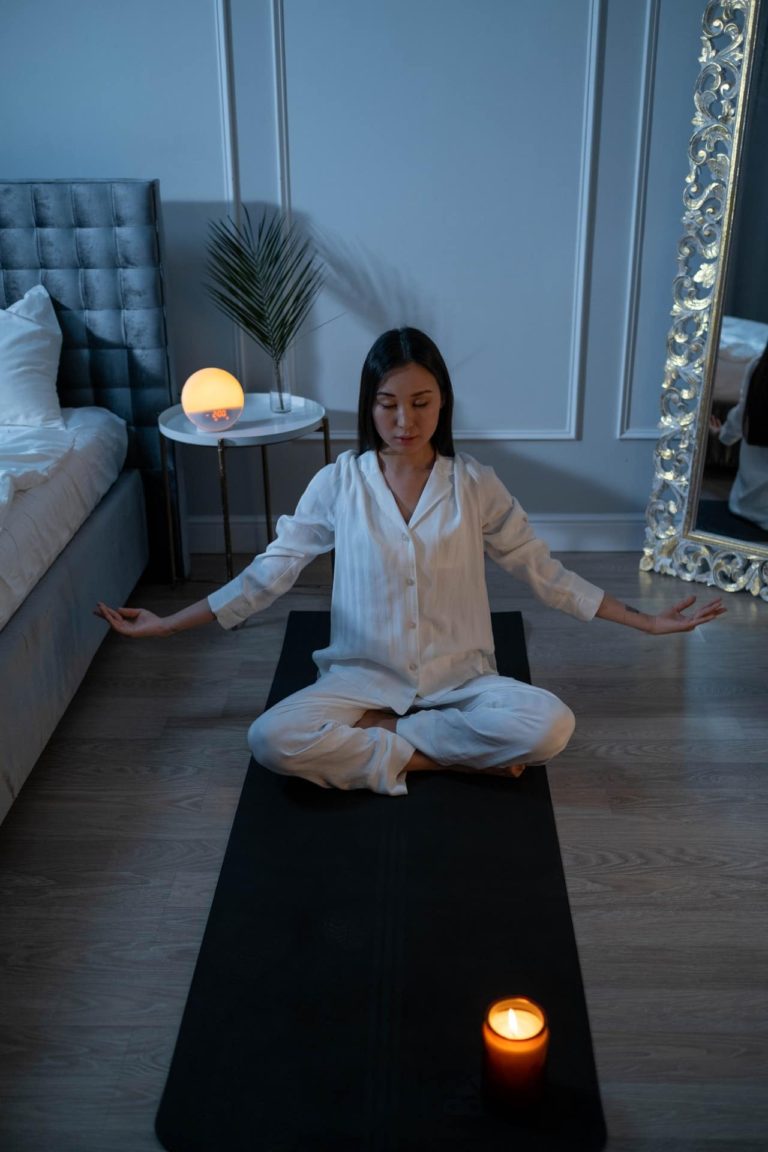 woman on a mat on the floor in her bedroom meditating with candles