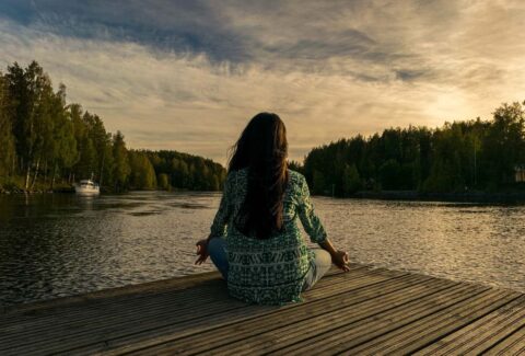 Woman meditating seated on a pier in front of a lake