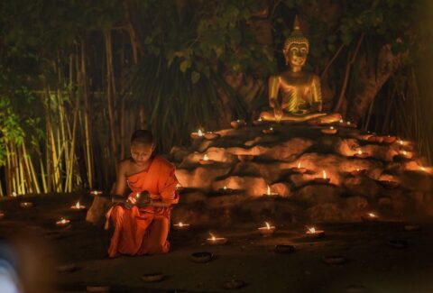 boy monk with candles and buddha statue behind him