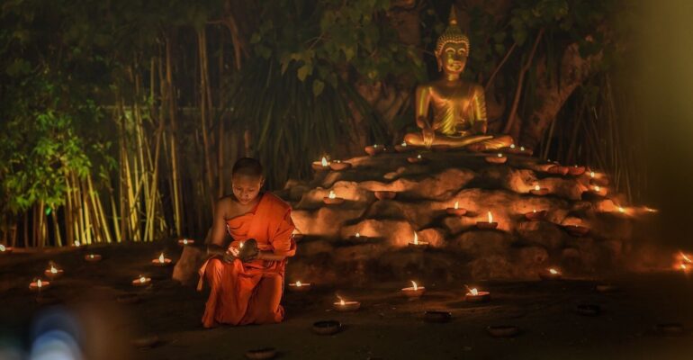 boy monk with candles and buddha statue behind him