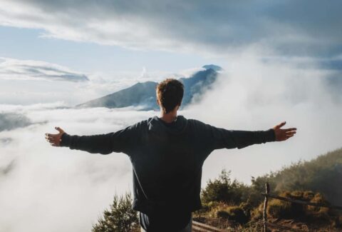 man opening hands on top of mountain clouds surrender to god