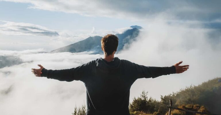 man opening hands on top of mountain clouds surrender to god
