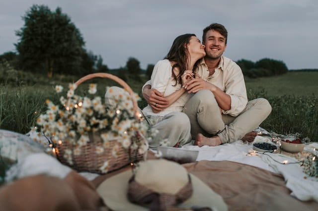 couple having picnic with basket of flowers in nature