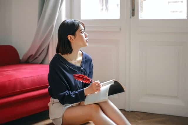 Woman looking through window writing on her journal about resentment