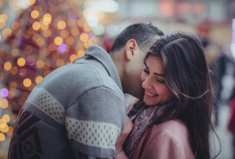 men kissing woman on cheek with lights behind them