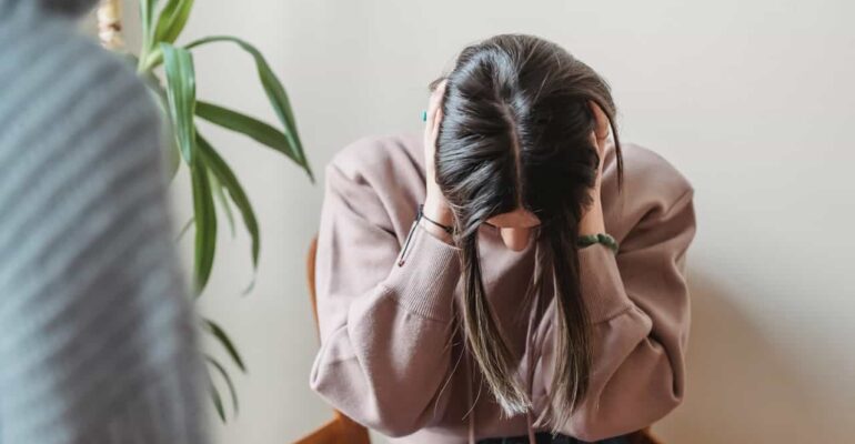 girl sitting down covering her ears to stop the negative chatter in her head