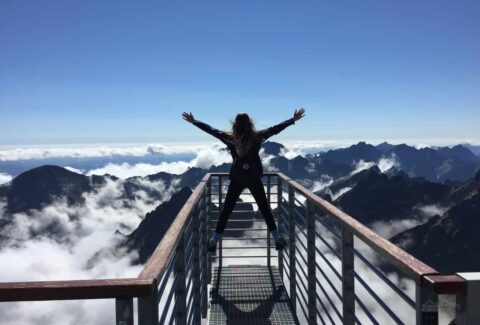 girl on bridge opening her arms up looking at the mountains and clouds