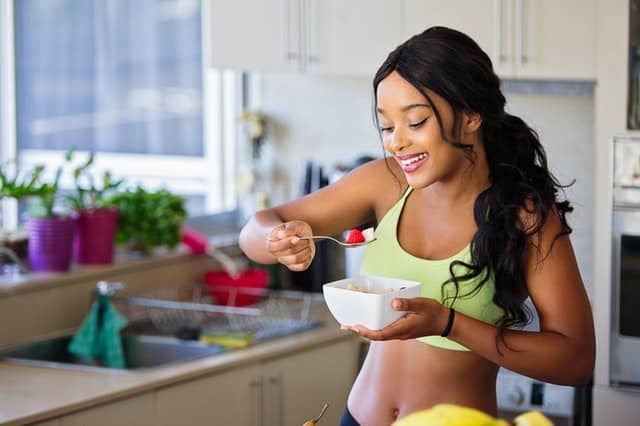 a woman in her gym clothes eating strawberry fruit and smiling at her food