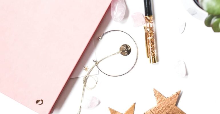 pink journal with gold stars, bracelet and glittery pen to manifest by writing