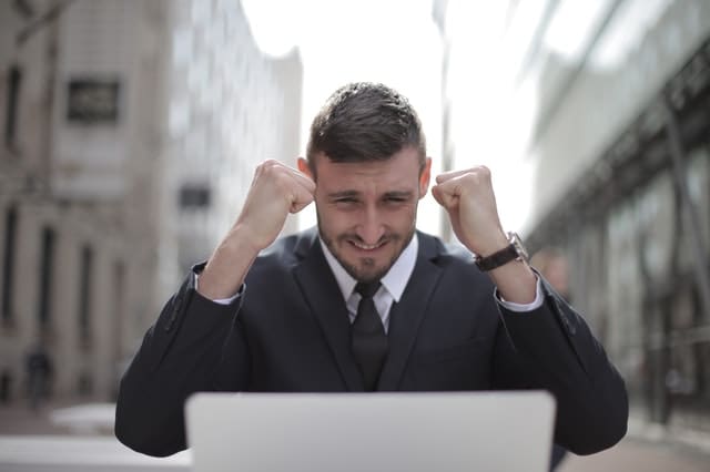 man wearing a suit wearing a watch smiling at his laptop outside in the road feeling confident