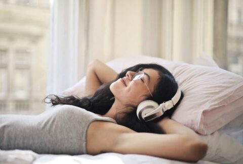 A girl on her bed smiling with headphones listening to music meditating
