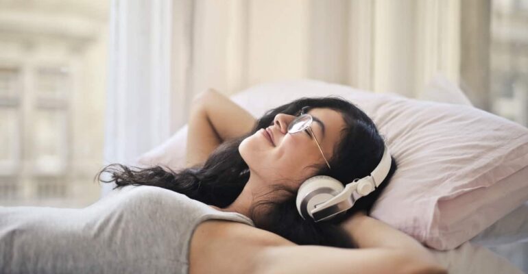 A girl on her bed smiling with headphones listening to music meditating