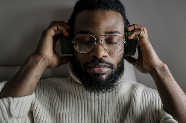 a man with glasses listening to music with headphones holding his headphones with his hands and closing his eyes