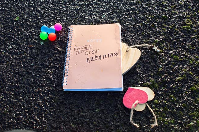 a pink notebook front cover written 'never stop dreaming' with a keychain next to it