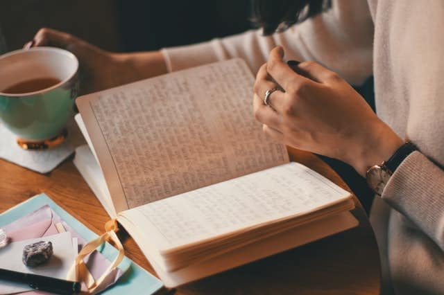 a girl on her desk with a cup of coffee reading her journal and written manifestations