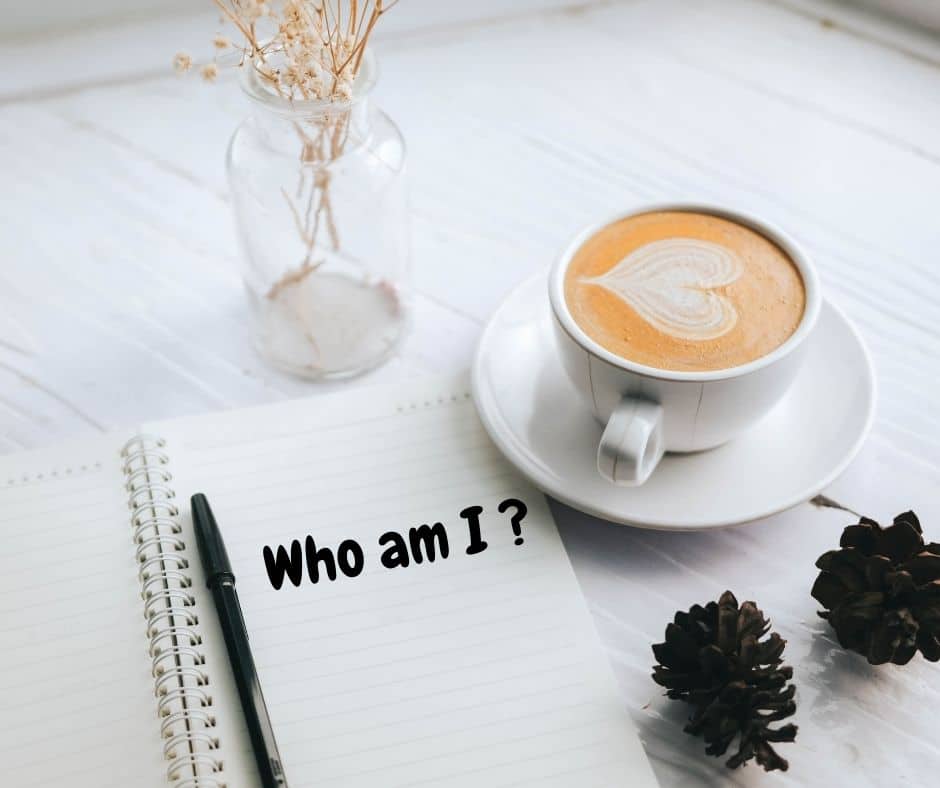 a cappuccino on a table next to a notebook with a black pen, with the words written: "who am I?' 