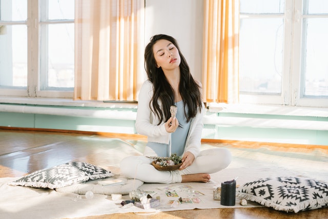 Woman meditating with cushions and crystals and sage to be open to receive abundance