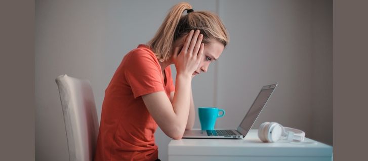 A girl on her desk with her laptop. Her hands are on her face she looks scared of failure in her career