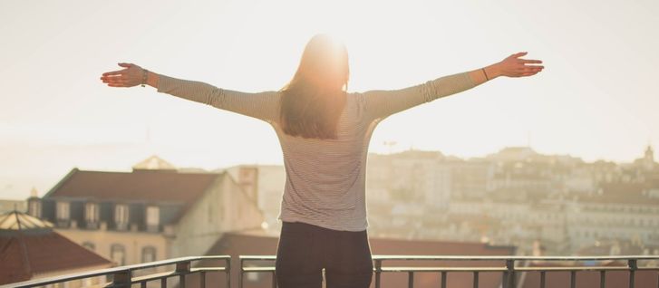 A woman in her balcony looking at a nice city view with her arms wide open living her life purpose