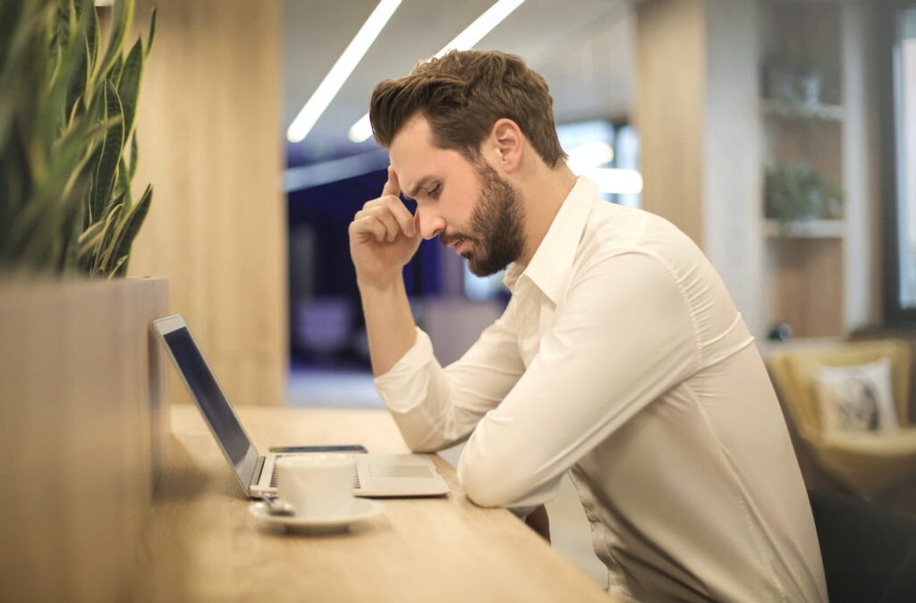 a guy at work feeling sad in the office looking down at his laptop