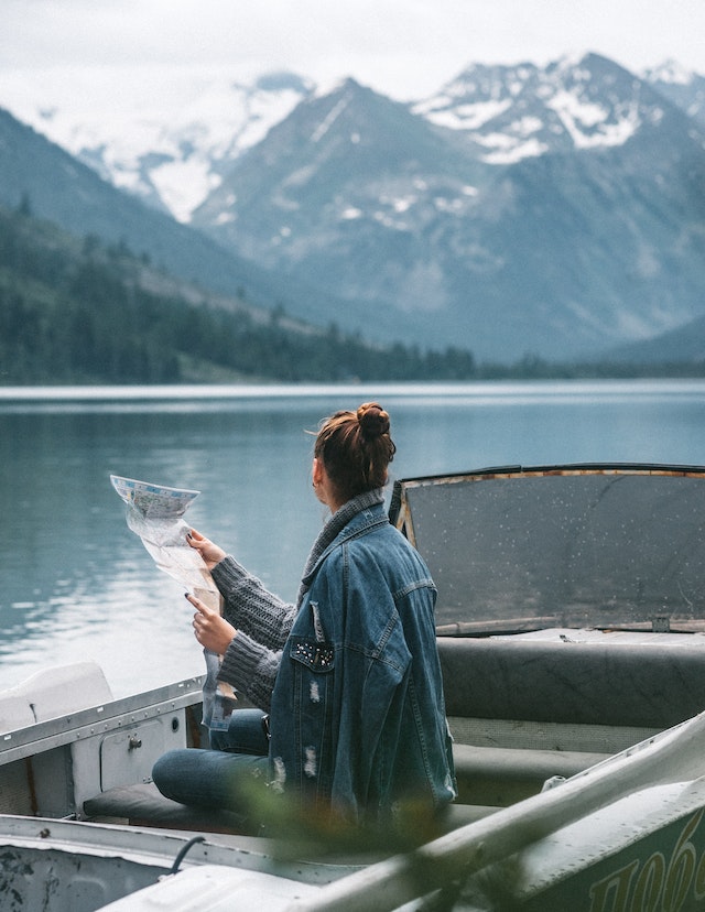 a woman on a boat looking at the mountains over a lake with a map in her hand as she embarks on a journey