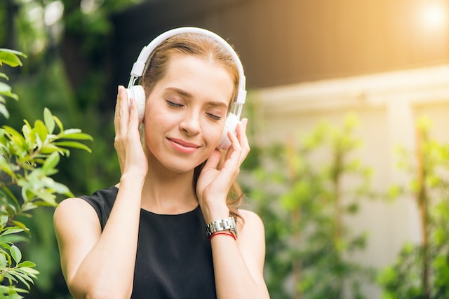 girl with eyes closed listening to music with headphones in nature to raise her vibration