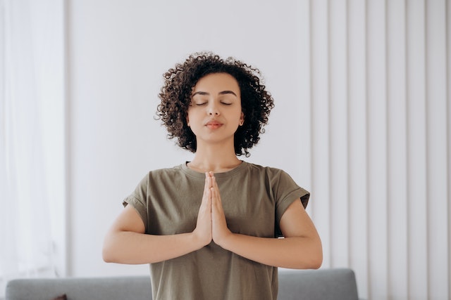 a girl with her eyes closed and hands in prayer practicing gratitude to raise her vibration for manifestation