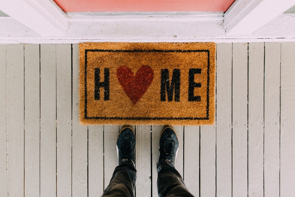 doormat with h<3me written on it and a guy standing next to it looking down at the doormat