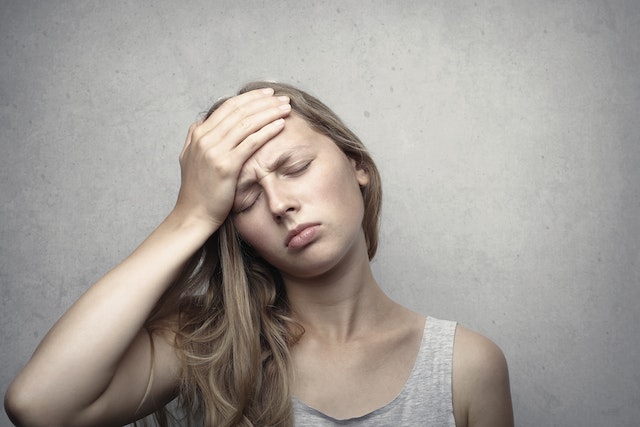 a girl with her hand on her forehead with eyes closed feeling upset due to blocked feminine energy