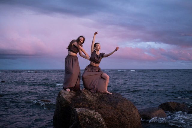 two young women doing an ecstatic dance on the rocks in front of the sea