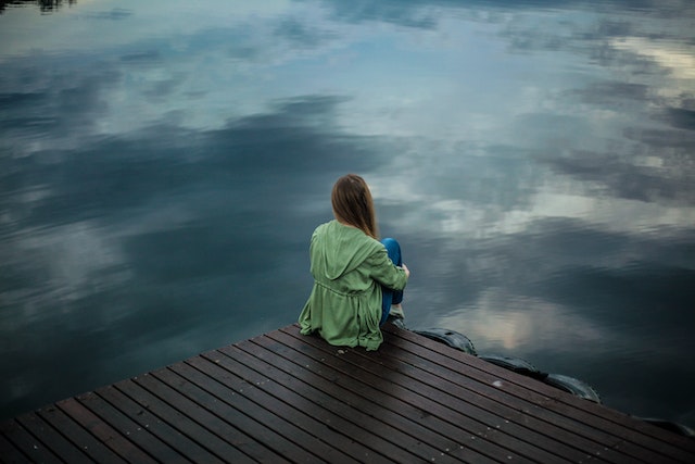 a girl sitting on the pier sitting down looking at the lake