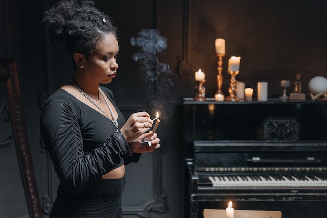 a woman dressed in a black dress lighting up a candle in a room with a piano and candles