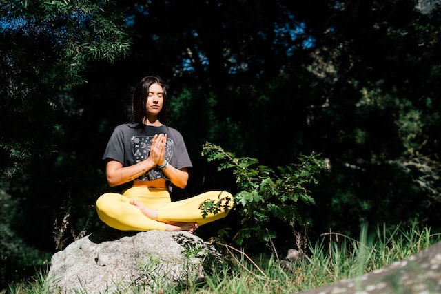 a girl meditating in nature on a rock with her eyes closed, hands in prayer, and yoga pants