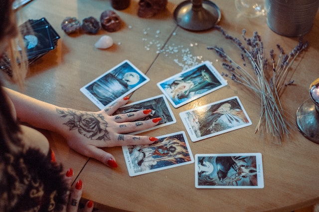 a girl with a tattoo on her hand and red nails with tarot cards on a desk with crystals and sage.jpg