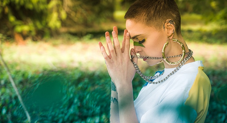 a girl in nature with cool jewelry, eyes closed head tilted down hands in prayer connecting with the divine and wondering is spirituality everything?