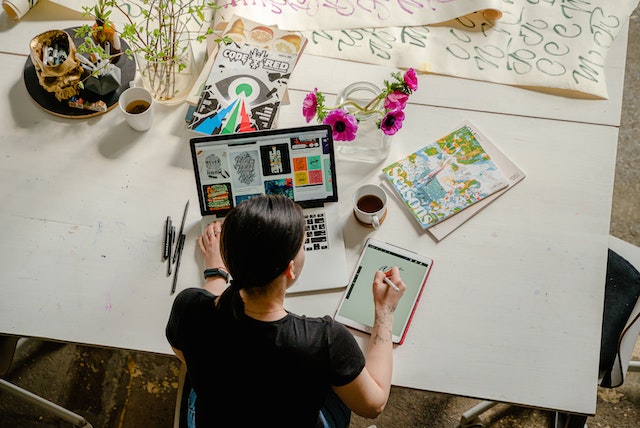 a girl on a desk with her laptop and tablet and art designs trying out her skills to discover her life purpose and what she's passionate about