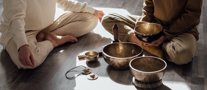 two people sitting on the floor in lotus position with sage and sound healing instruments for meditation and spiritual mentoring