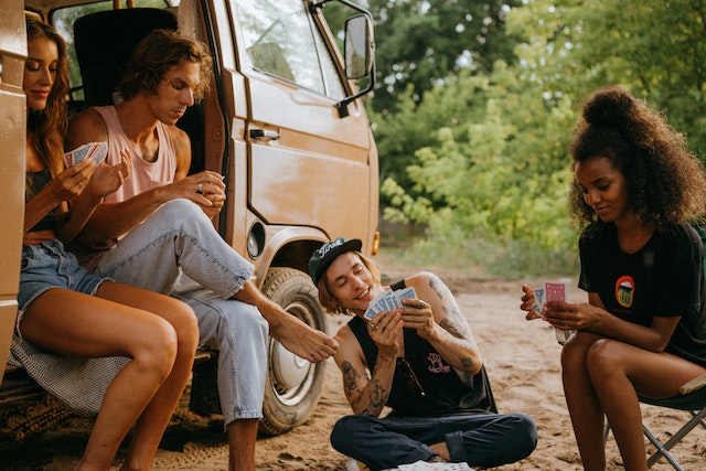 a group of friends in nature in a caravan playing cards and demonstrating different emotions in a socially aware group