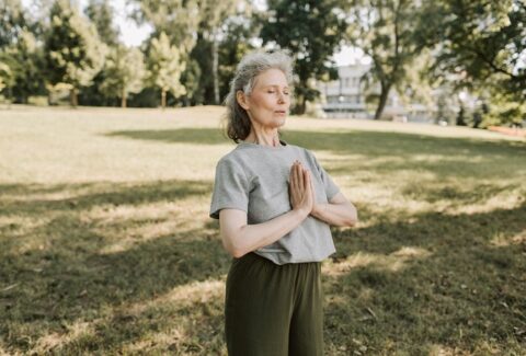 50 year old woman in the park hands in prayer mode, eyes closed, connecting with her spiritual self to find purpose in life after 50